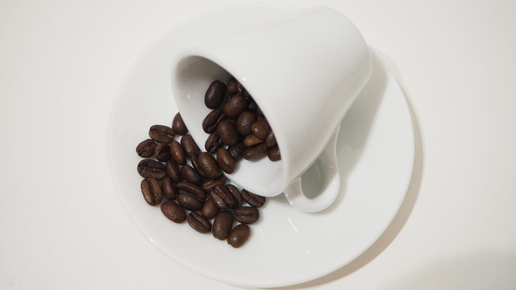 デミタスカップからコーヒー豆がこぼれている写真